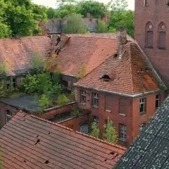 Opuszczony **szpital psychiatryczny** z rozpadającymi się dachami i zarośniętymi dziedzińcami, idealne miejsce na **horror o szpitalu psychiatrycznym**.