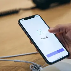 Dłoń trzyma smartfon z włączonym ekranem, na którym widnieje ikona i napis Face ID.
