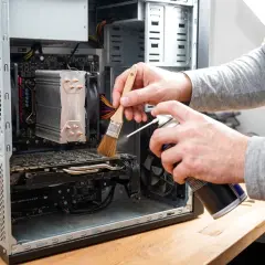 Czyszczenie komputera: ręce z pędzelkiem i sprężonym powietrzem usuwają kurz z wnętrza obudowy PC.