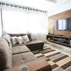 Nowoczesny salon z brązową kanapą, telewizorem na drewnianej ścianie i dywanem. Idealny przykład, jaki uchwyt do telewizora wybrać, by stworzyć taką przestrzeń.