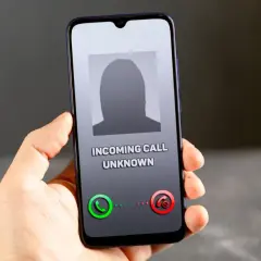 Dłoń trzyma smartfon z ekranem pokazującym przychodzące połączenie od nieznanego numeru. Brak ID dzwoniącego.