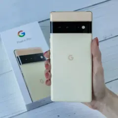 Dłoń trzyma kremowy telefon Pixel 6 Pro, obok pudełko z tymi samymi telefonami z czystym Androidem.