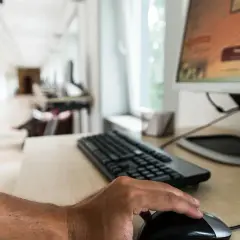 Dłoń na myszce przed monitorem. Komputer z zintegrowaną kartą graficzną działa sprawnie w biurze.