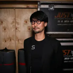 Hideo Kojima, mistrz gier wideo, w otoczeniu sprzętu, jakby przygotowywał się do kolejnej epickiej przygody.