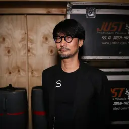 Hideo Kojima, mistrz gier wideo, w otoczeniu sprzętu, jakby przygotowywał się do kolejnej epickiej przygody.