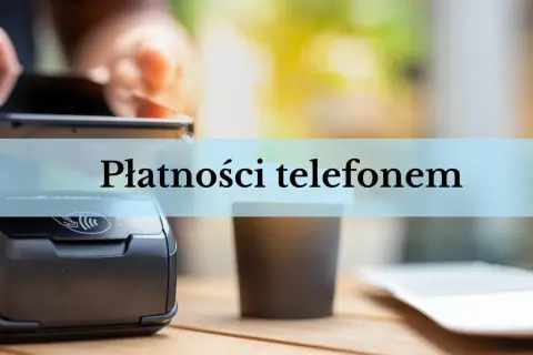 Zbliżenie na terminal płatniczy i kubek kawy. Dłoń trzyma smartfon, gotowa do płatności telefonem.