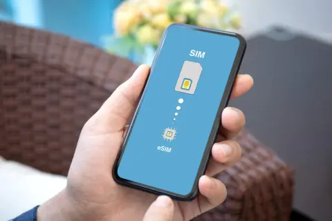 Dłoń trzyma smartfon z ekranem pokazującym przejście od tradycyjnej karty SIM do technologii eSIM.