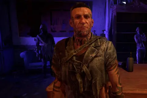 Damien z Dying Light 2, z tatuażami na twarzy i szyi, stoi w ponurym pomieszczeniu.