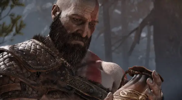 Kratos z brodą i czerwonymi znakami na twarzy, w zbroi, trzyma sakiewkę. Dzieło Santa Monica Studio.