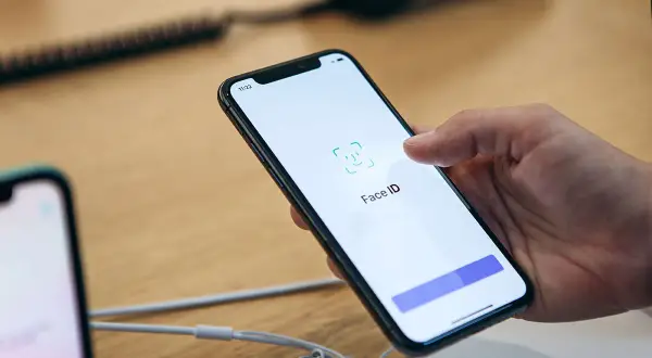 Dłoń trzyma smartfon z włączonym ekranem, na którym widnieje ikona i napis Face ID.