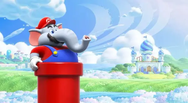 Słoń Mario z serii Super Mario wychyla się z czerwonej rury na tle bajkowej krainy z zamkiem.