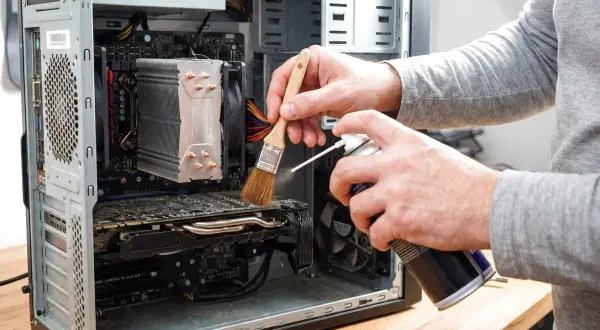 Czyszczenie komputera: ręce z pędzelkiem i sprężonym powietrzem usuwają kurz z wnętrza obudowy PC.