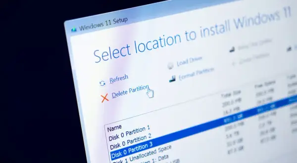 Instalator Windows 11 pokazuje opcje zarządzania partycjami. Kursor myszy wskazuje "Usuń partycję", przygotowując do formatowania dysku.