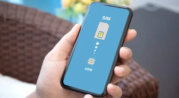 Dłoń trzyma smartfon z ekranem pokazującym przejście od tradycyjnej karty SIM do technologii eSIM.