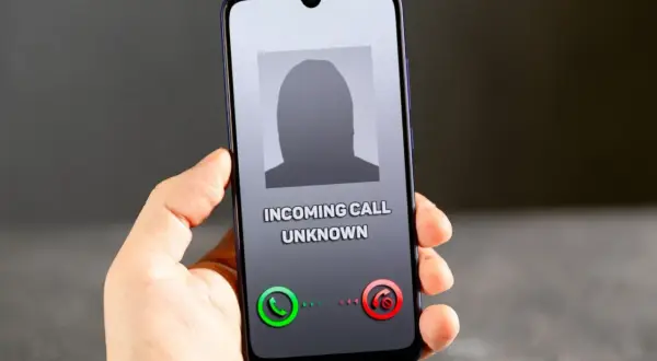 Dłoń trzyma smartfon z ekranem pokazującym przychodzące połączenie od nieznanego numeru. Brak ID dzwoniącego.