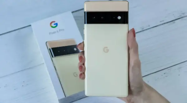 Dłoń trzyma kremowy telefon Pixel 6 Pro, obok pudełko z tymi samymi telefonami z czystym Androidem.