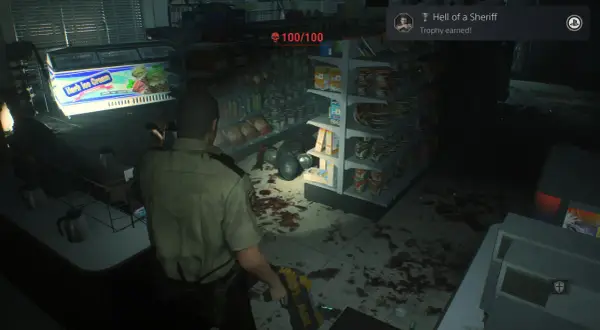 Policjant w sklepie, gdzie widać plamy krwi i półki z produktami. Osiągnięto trofea Resident Evil 2 "Hell of a Sheriff".