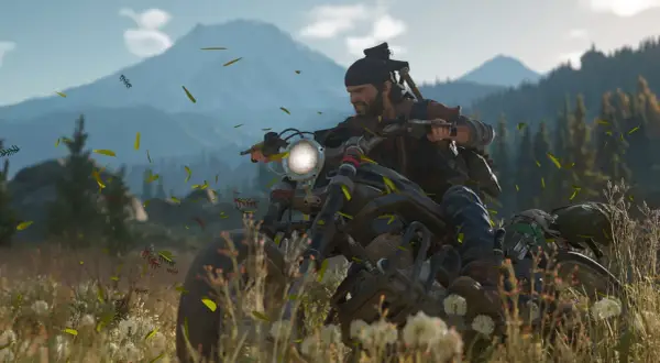 Deacon z Days Gone 2 pędzi motocyklem przez łąkę, a wokół latają liście.