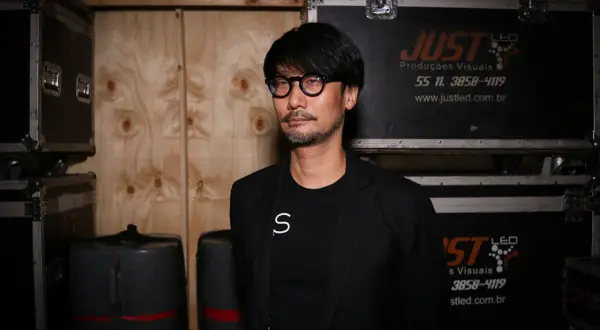 Hideo Kojima, mistrz gier wideo, w otoczeniu sprzętu, jakby przygotowywał się do kolejnej epickiej przygody.
