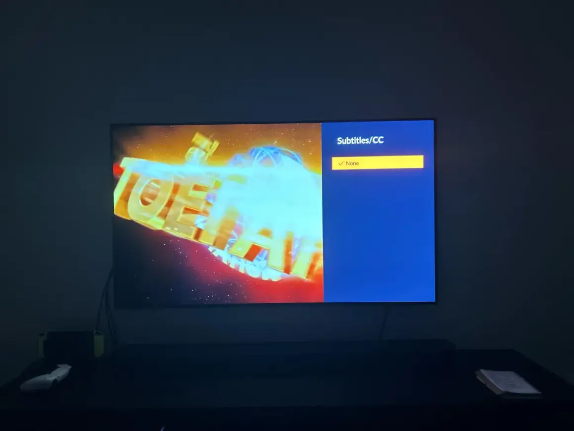 Na ekranie telewizora logo anime z niebieskimi napisami. Menu wyboru napisów pokazuje "None", ale szukam opcji "crunchyroll polskie napisy".