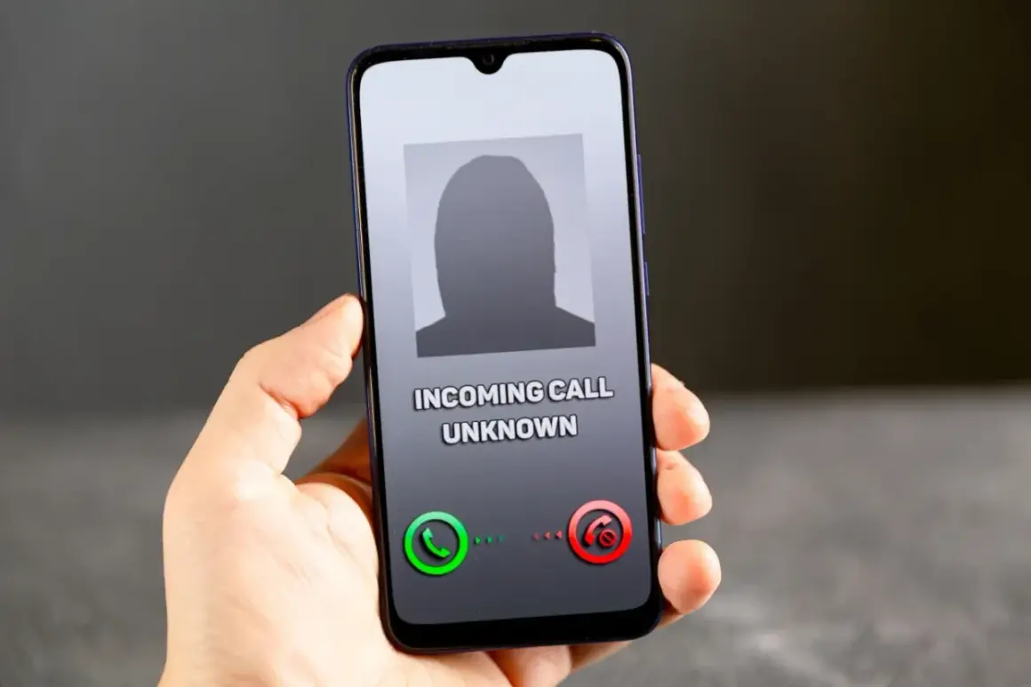 Dłoń trzyma smartfon z ekranem pokazującym przychodzące połączenie od nieznanego numeru. Brak ID dzwoniącego.