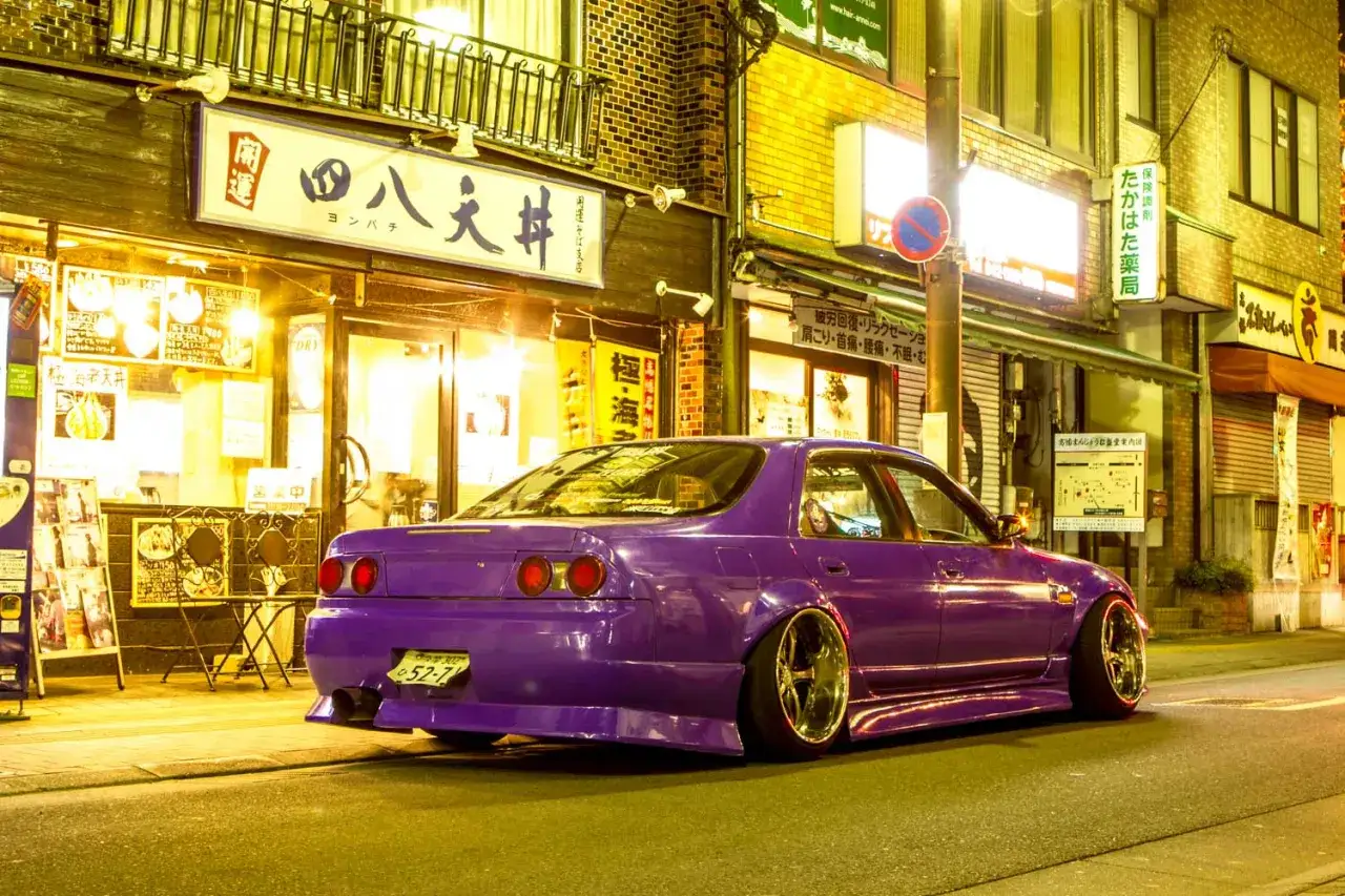 Fioletowy Nissan Skyline, jdm japanese drift master, parkuje nocą przed japońską restauracją.