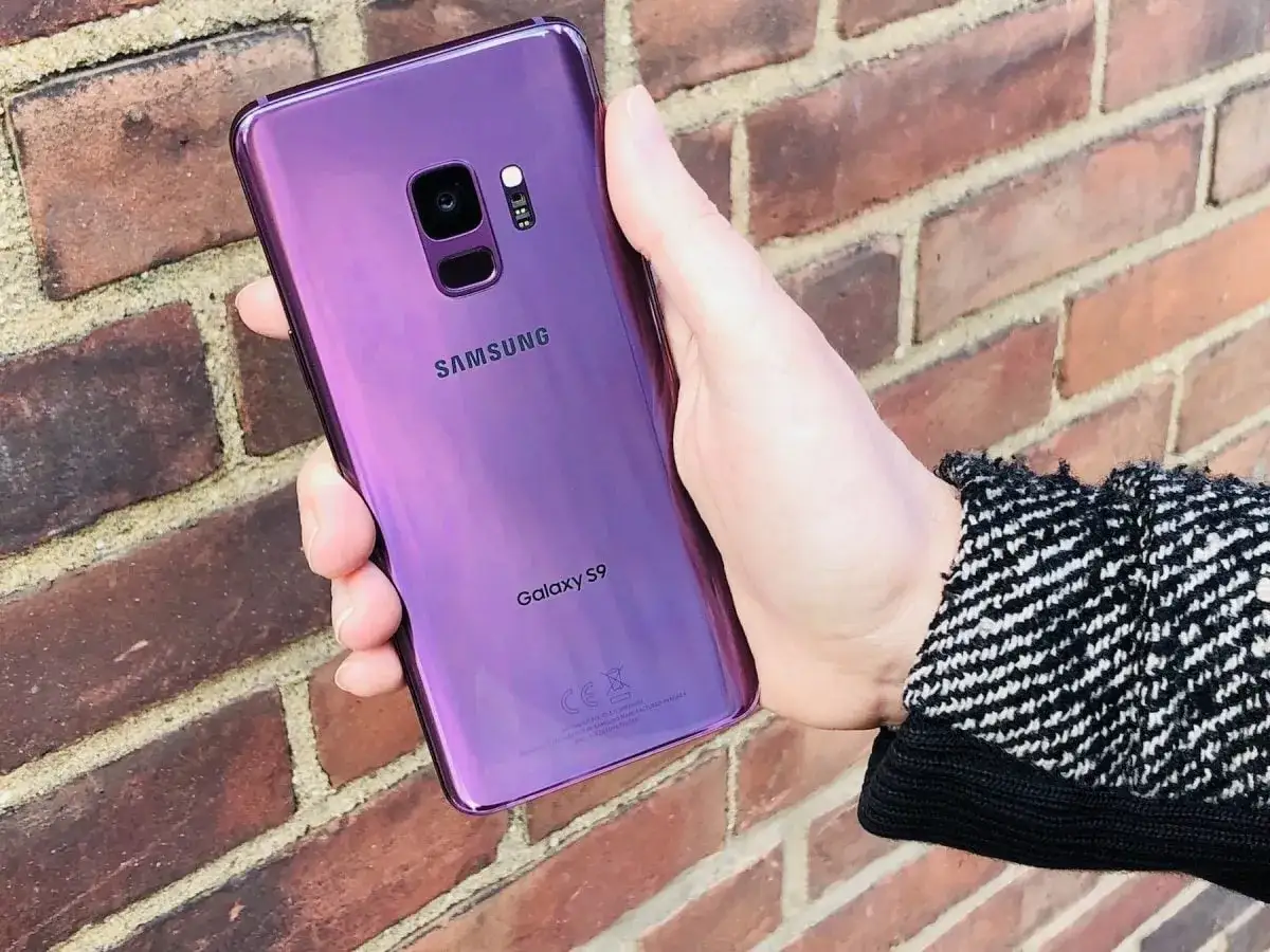 Fioletowy Samsung Galaxy S9 w dłoni, tuż po premierze. Ceglana ściana w tle.