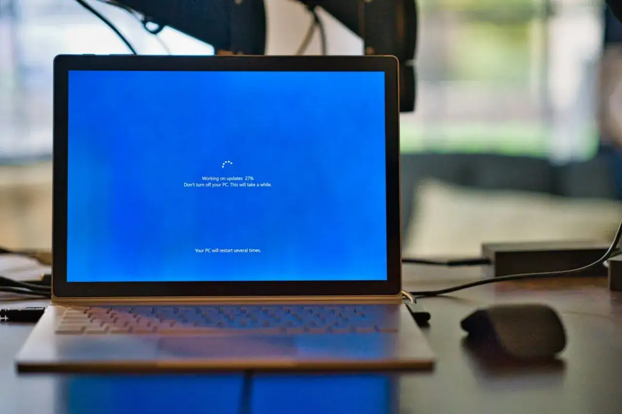 Laptop z niebieskim ekranem Windows, na którym trwa aktualizacja. Proces
