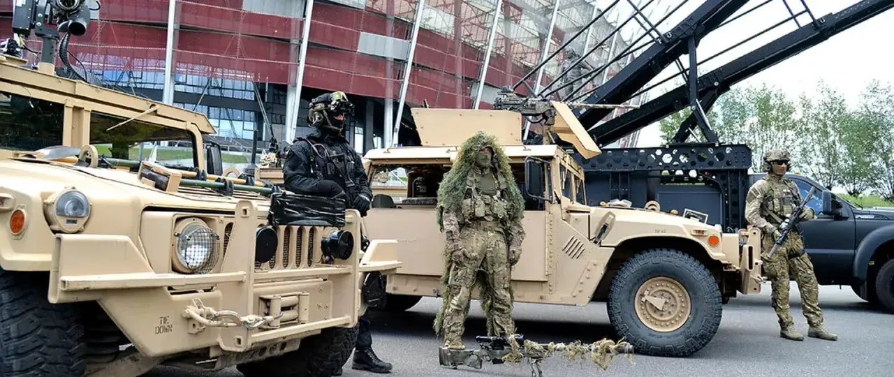 Żołnierze w kamuflażu i oporządzeniu, obok pojazdów wojskowych. Sprzęt spełnia standard militarny mil-std-810h.