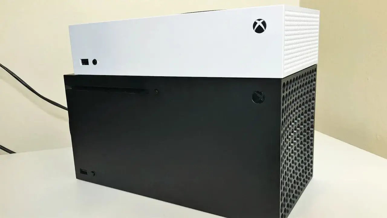 Dwie konsole Xbox: czarna na dole i biała na górze. Widoczne logo Xbox i otwory wentylacyjne.