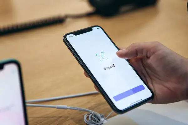 Dłoń trzyma smartfon z włączonym ekranem, na którym widnieje ikona i napis Face ID.