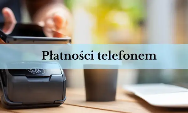 Zbliżenie na terminal płatniczy i kubek kawy. Dłoń trzyma smartfon, gotowa do płatności telefonem.