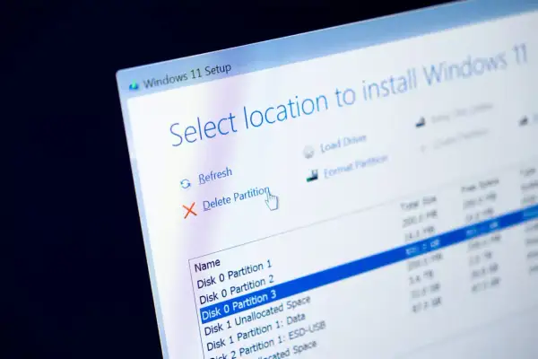 Instalator Windows 11 pokazuje opcje zarządzania partycjami. Kursor myszy wskazuje "Usuń partycję", przygotowując do formatowania dysku.
