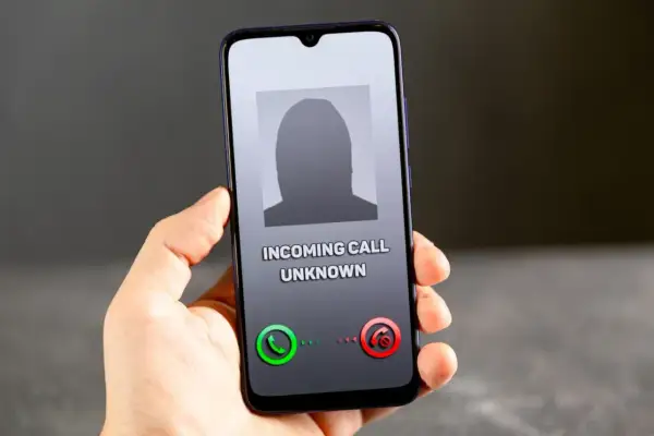 Dłoń trzyma smartfon z ekranem pokazującym przychodzące połączenie od nieznanego numeru. Brak ID dzwoniącego.
