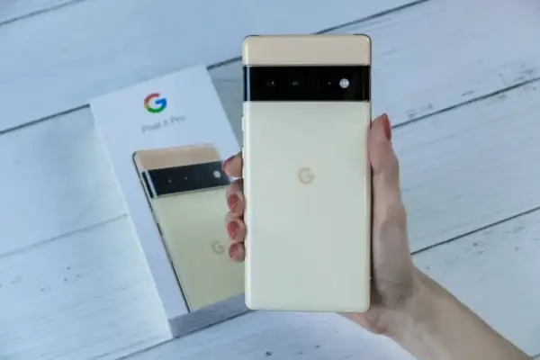 Dłoń trzyma kremowy telefon Pixel 6 Pro, obok pudełko z tymi samymi telefonami z czystym Androidem.