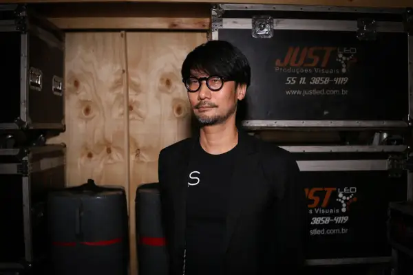 Hideo Kojima, mistrz gier wideo, w otoczeniu sprzętu, jakby przygotowywał się do kolejnej epickiej przygody.
